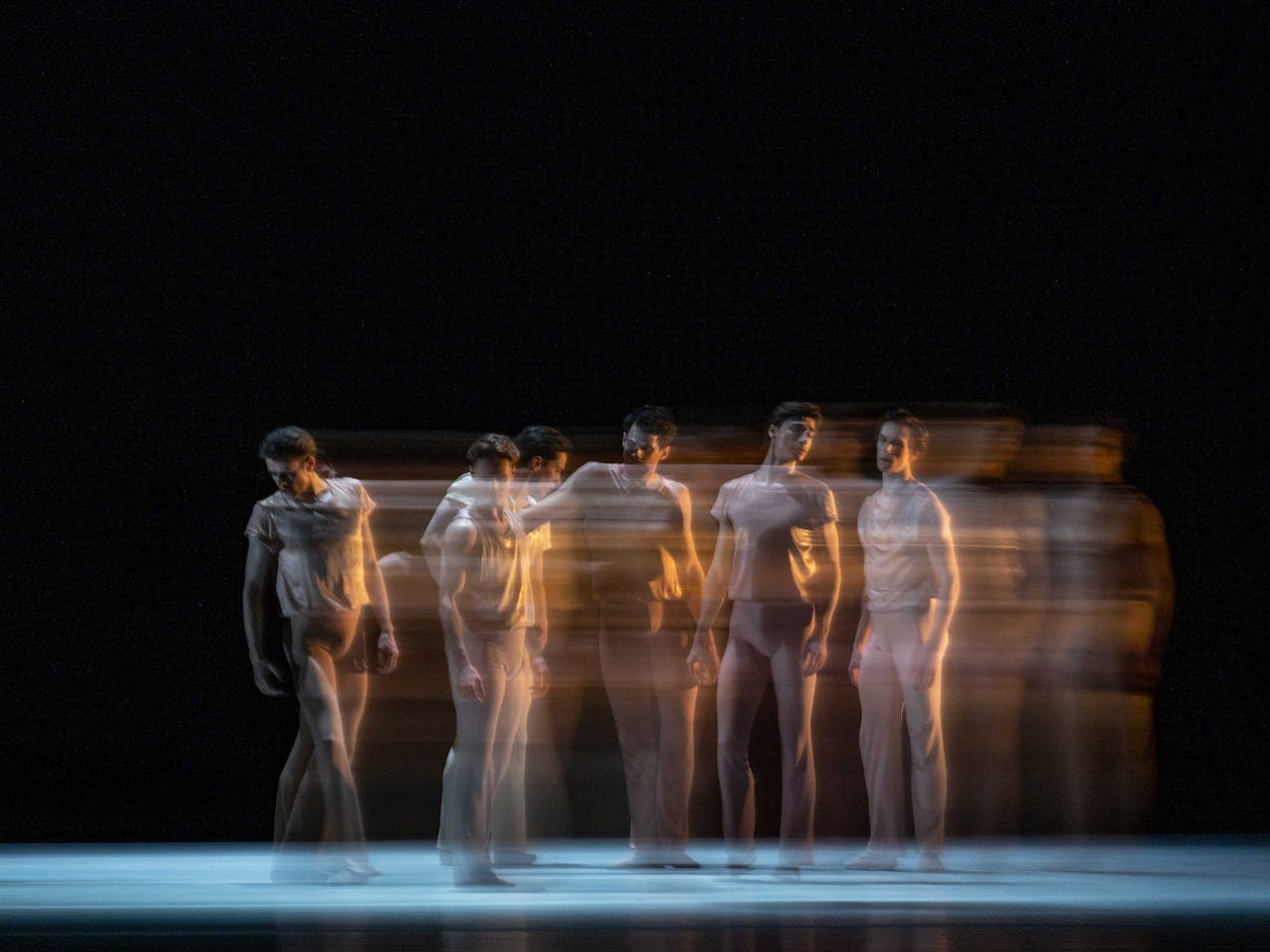 five dancers stand tall. The way the photograph has been taken makes them look like they are in motion as their bodies blur. 