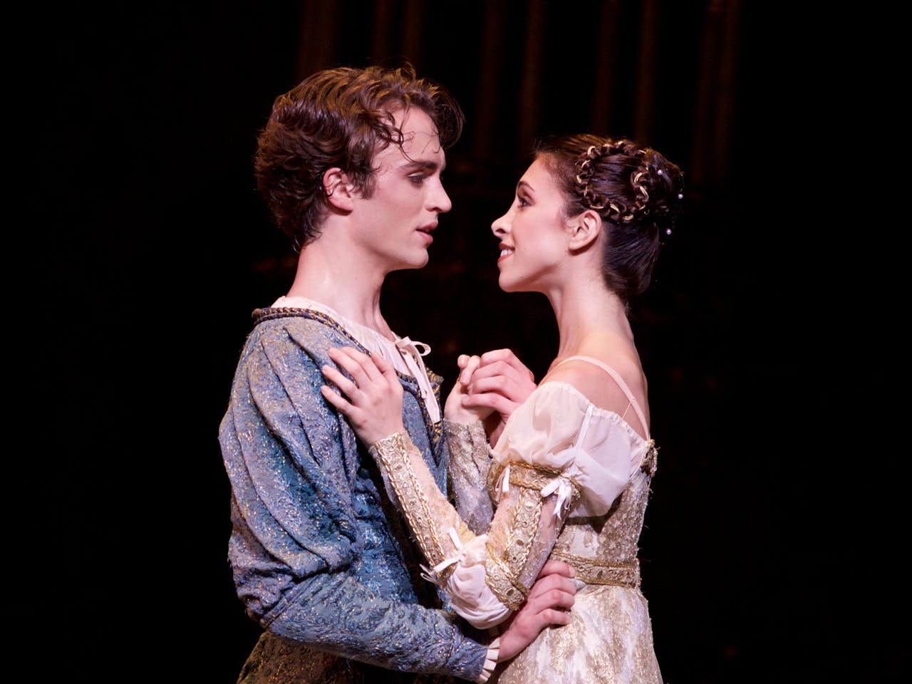 Two ballet dancers perform on stage: they are staring into each others eyes and embracing.