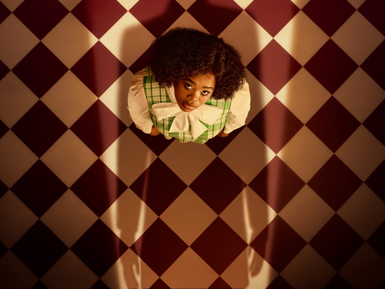 Opera singer Pretty Yende is photographed as Semele, a character from the opera of the same name. Semele is viewed from above, as she gazes at someone who casts a looming shadow over her.
