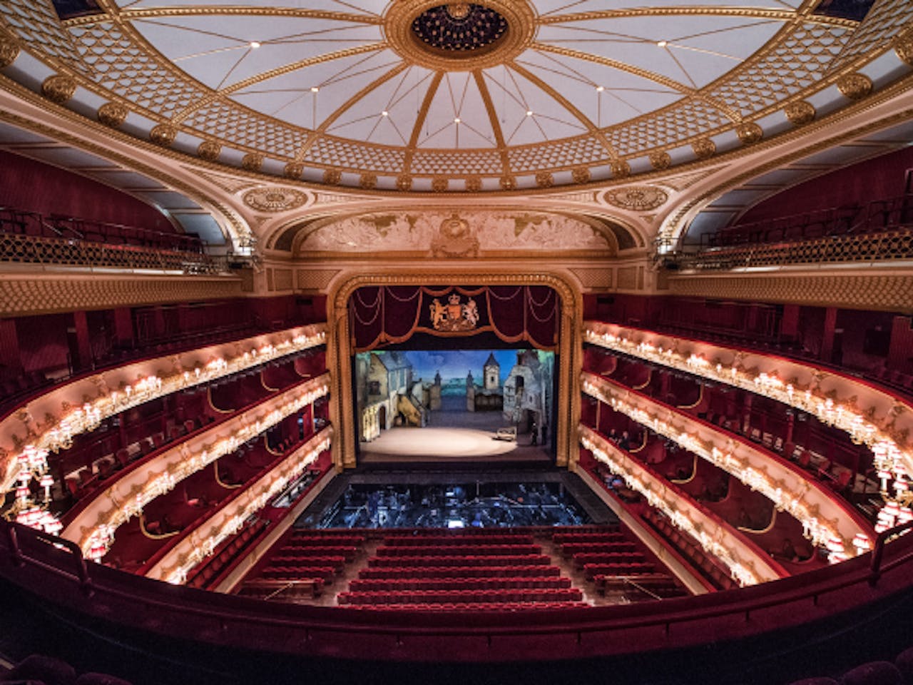 A view looking down at the seating, stage and circular ceiling the auditorium of the Royal Opera House