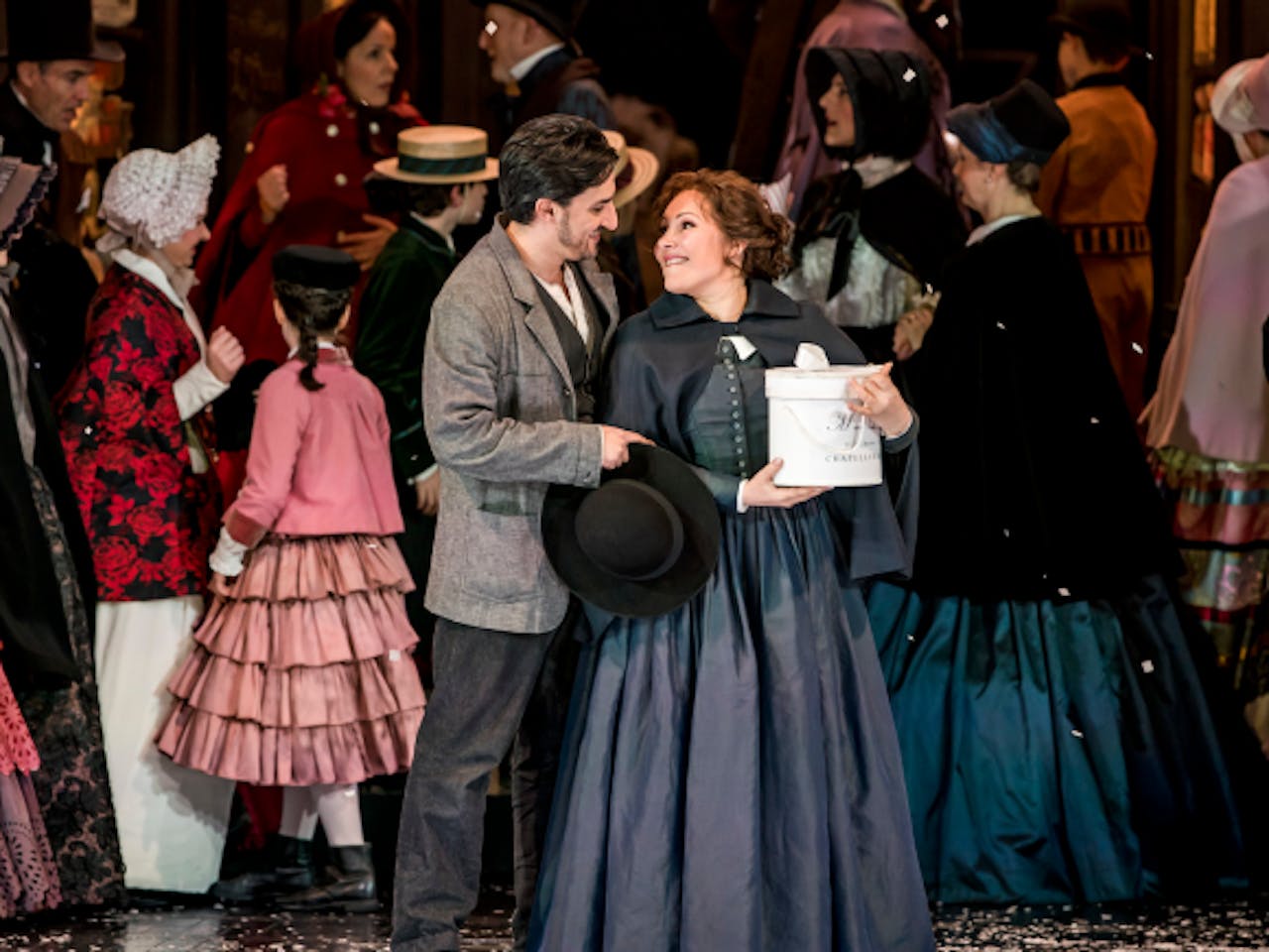 A couple stand in the centre of a happy crowd looking at each other lovingly.