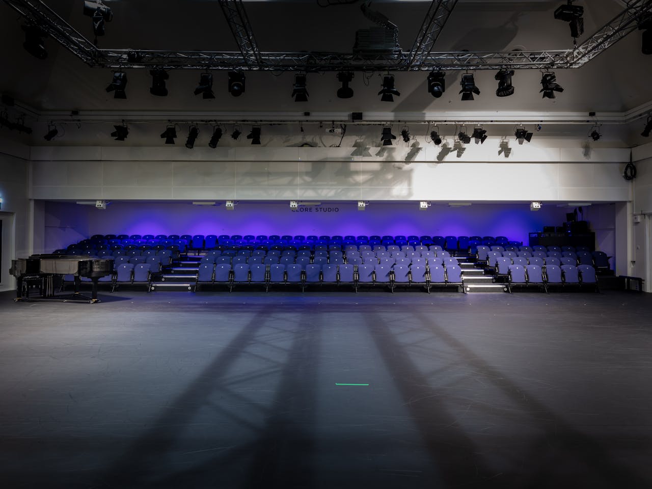 A view looking at the seating of the Clore Studio at the Royal Opera House, which is lit up with purple lighting