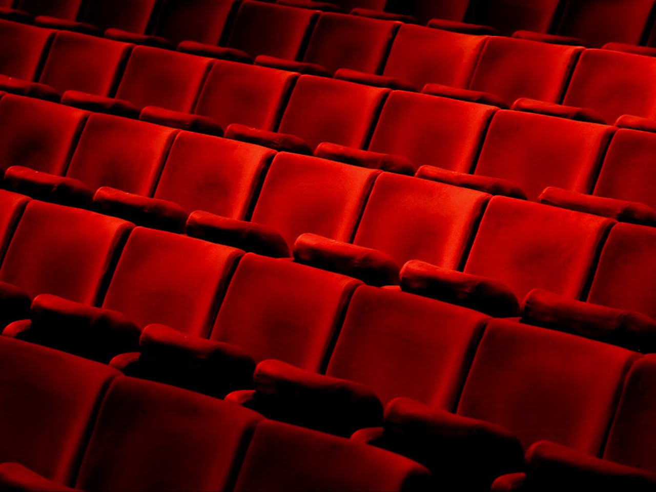 Five rows of vibrant red velvet theatre chairs with arm rests