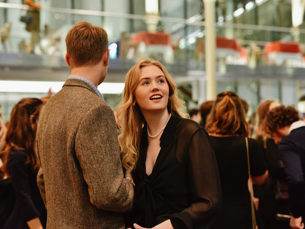Two young people conversing in a crowd at the Royal Opera House.