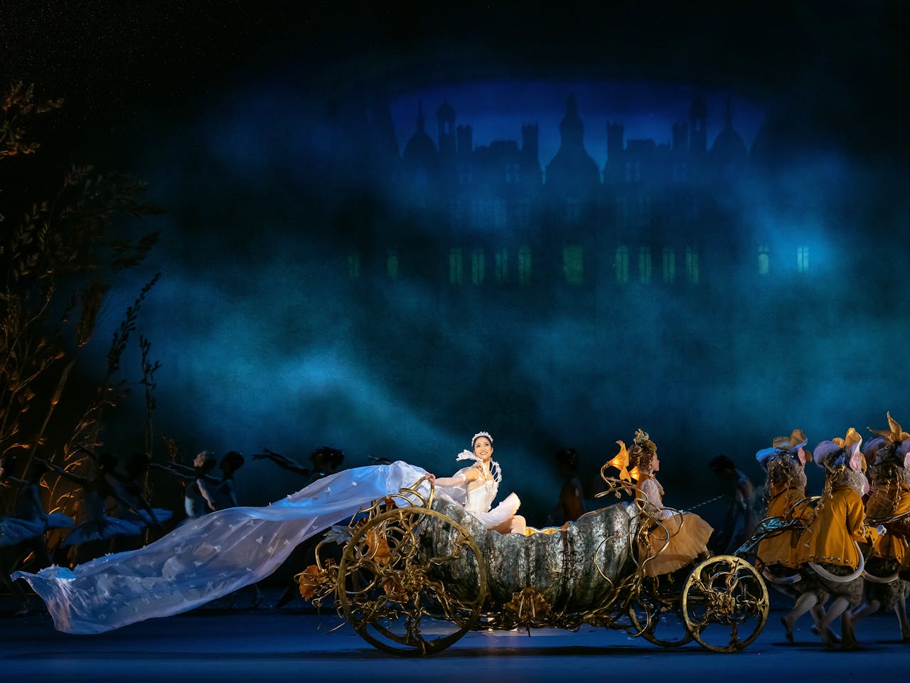 An elaborate carriage sits in the centre of the stage as a performer in a ballgown looks out at the audience. 