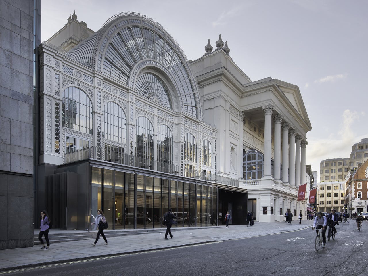 An image of the Royal Opera House from Bow Street - a large glass fronted building next to a traditional building with six columns