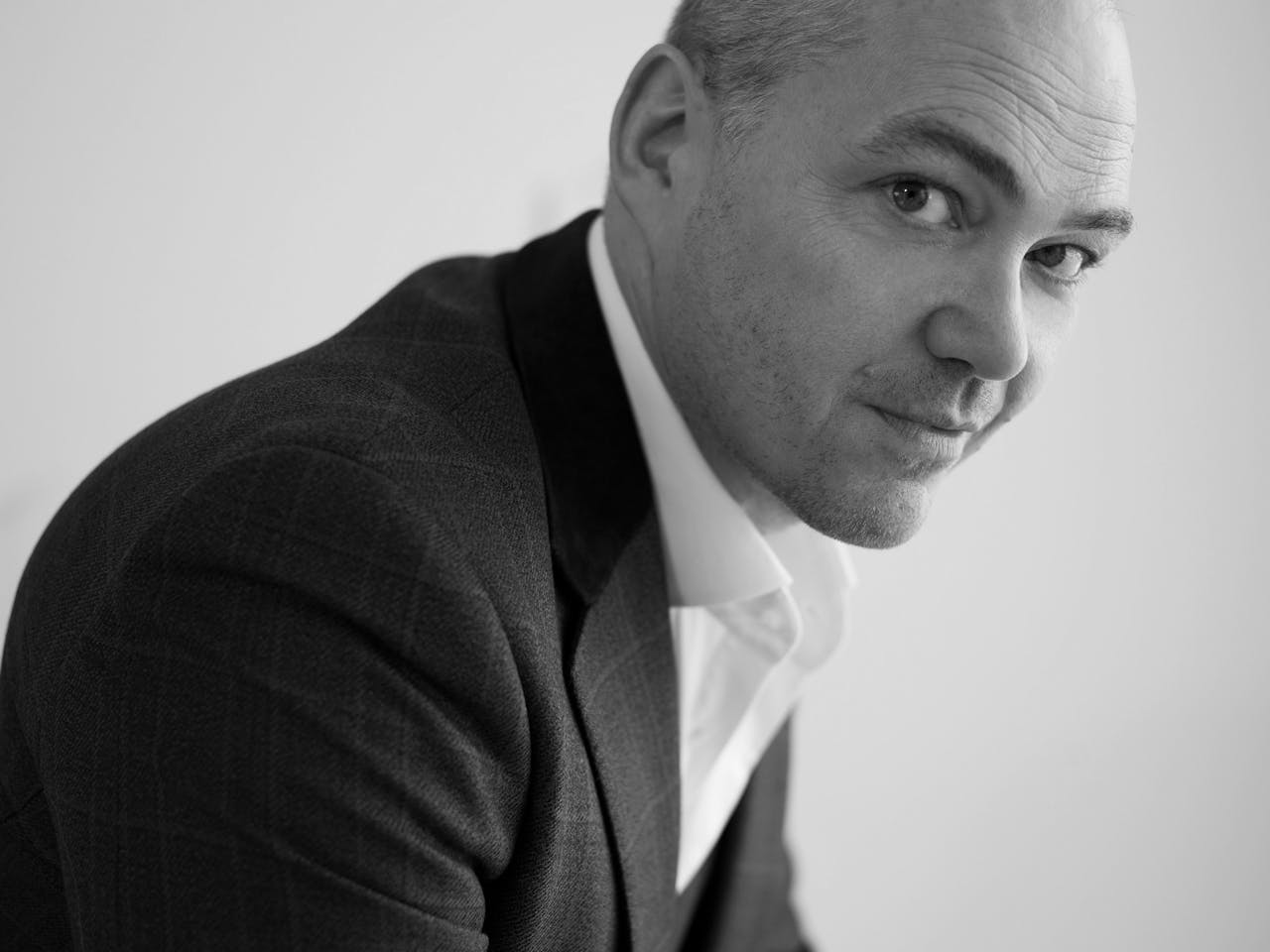 A black and white headshot - the side profile of a person looking straight at the camera. They are wearing a black suit and white shirt.