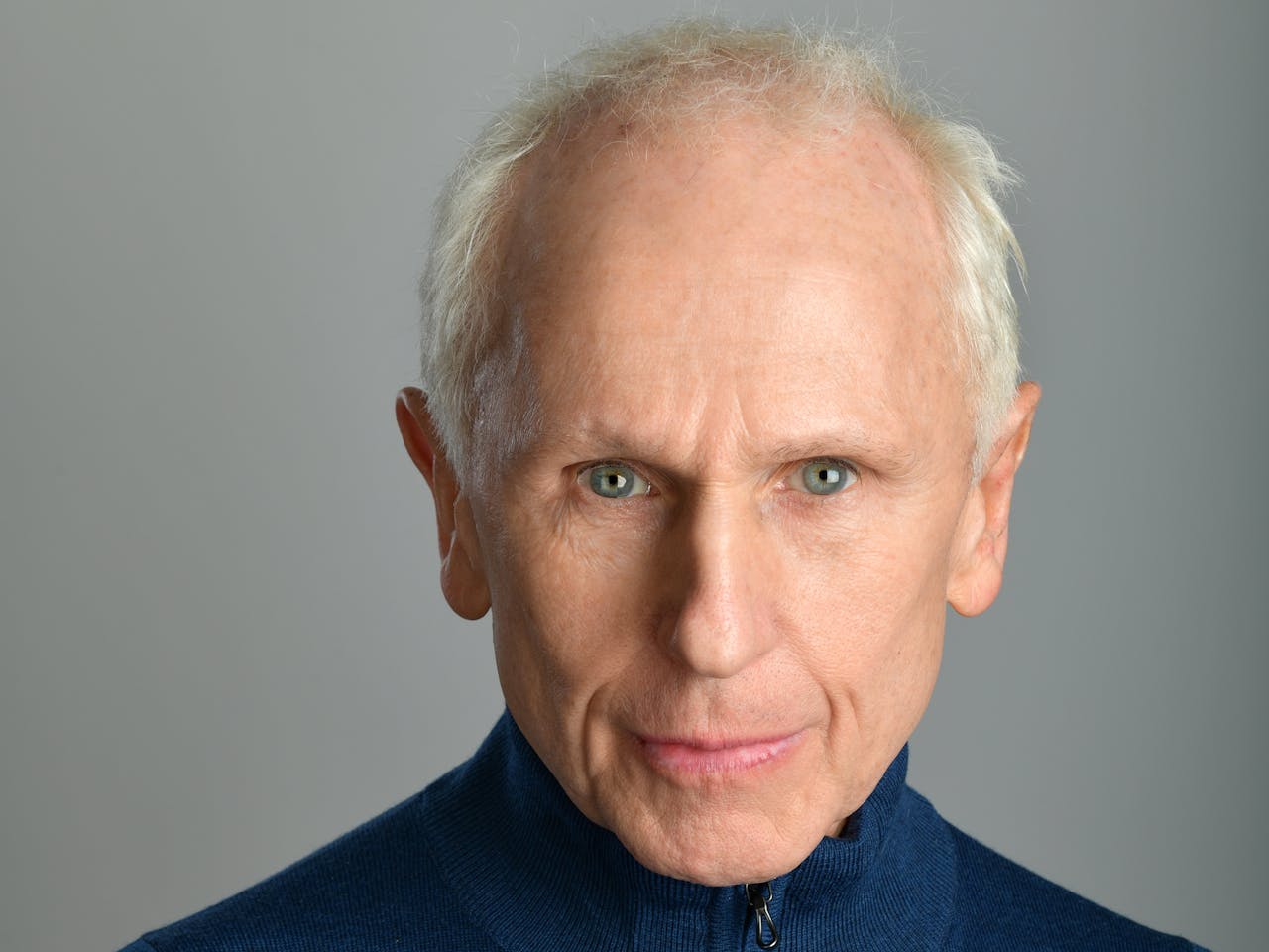 A headshot photograph of dancer Wayne Sleep. He is wearing a blue rollneck sweater and has his arms crossed.